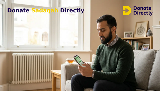 UK Muslim man donating sadaqah on phone in a bright living room to support a mosque
