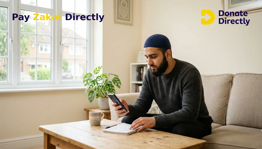 British Muslim man calculating Zakat on crypto using phone in a bright UK living room