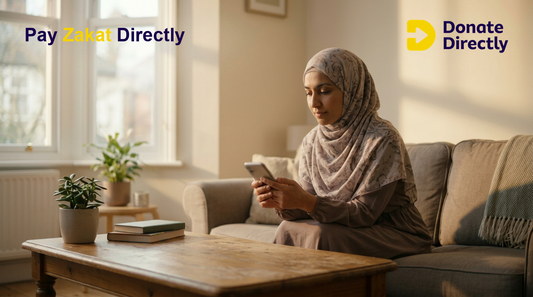 Muslim donor in a UK living room paying Zakat on a phone with a calm focused expression.