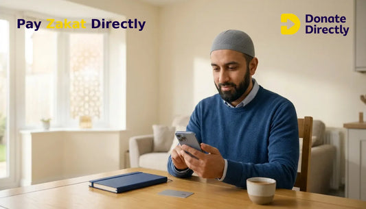 British Muslim father paying Zakat on a phone in a bright UK home.