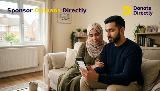 British Muslim couple in a bright UK home setting up orphan sponsorship on a smartphone