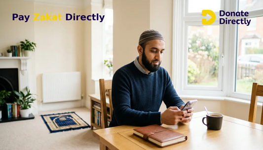 British Muslim man calculating Zakat on his phone in a bright UK home