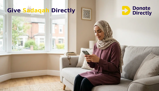 British Muslim woman giving Sadaqah privately on her phone in a bright UK living room