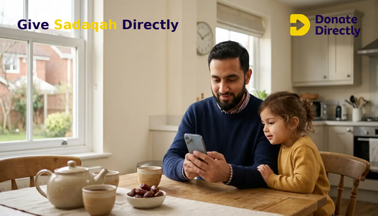 British Muslim father giving Sadaqah online at home while his child watches.